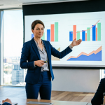 Бизнес-тренер в деловом костюме показывает графики и диаграммы на экране презентации коллегам в современном конференц-зале